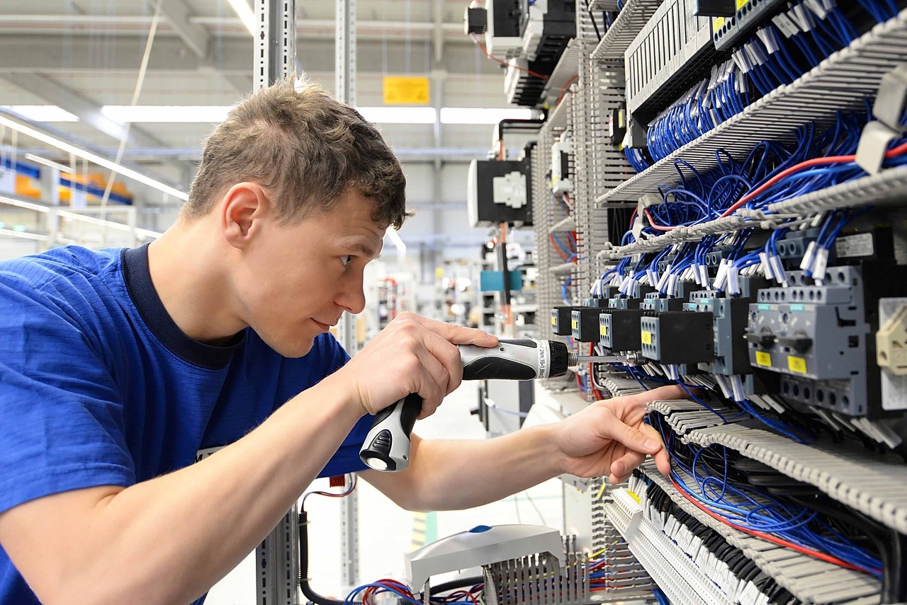 young operator assembles machine in a modern high tech factory - production of switch cabinets for industrial plant